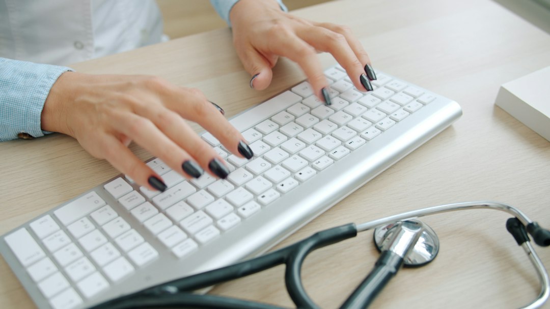Illustrative healthcare professional using a computer at a desk to review medical documentation